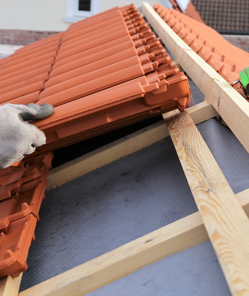 Pose de tuiles en terre cuite: installation de couverture de toit. Pose de tuiles en terre cuite par un couvreur. Liteaux de bois neufs et écran de sous-toiture gris lors de la construction du toit.