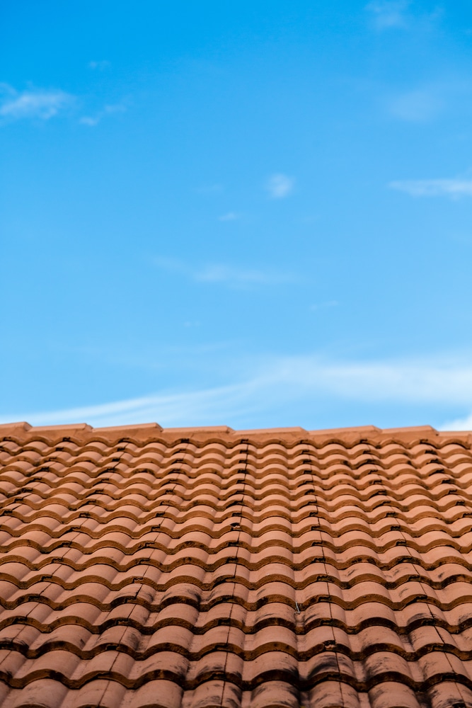 Toit en Tuiles Terre Cuite sous un Ciel Bleu | Habitat Toit en tuiles de terre cuite ondulées sous un grand ciel bleu clair avec de légers nuages.